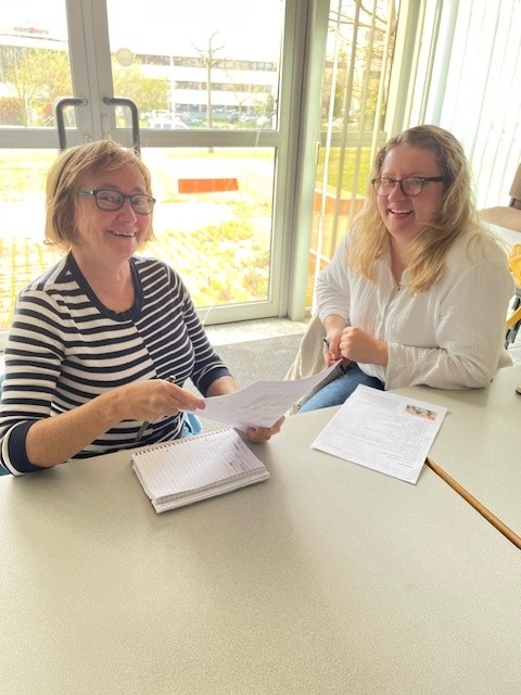 On voit deux femmes qui suivent un cours de français et qui semblent heureuses